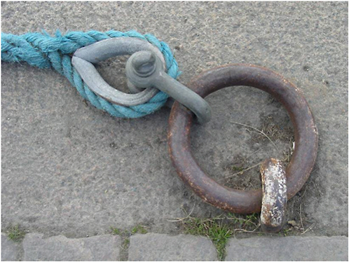 FIGURE 1.1 A mooring ring, shackle, and thimble with rope illustrate three different techniques for combatting the effects of materials degradation,. Originally, the ring and eye bolt were painted, the shackle and thimble were galvanized (zinc coated), and the mooring line was made of nylon. Courtesy of Erik Svedberg.