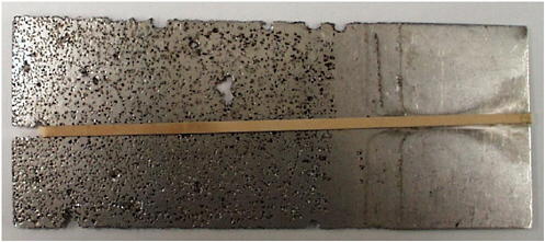 FIGURE 3.8 Acid-induced pitting and crevice corrosion of a stainless steel alloy exposed to ferric chloride (note the corrosion under the rubber band at left—left side dipped). SOURCE: University of Virginia Center for Electrochemical Science and Engineering, courtesy of John R. Scully.